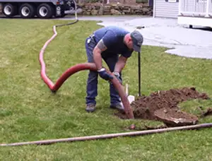 Septic pumping technician servicing a residential septic tank with a vacuum hose in Evansville, IN