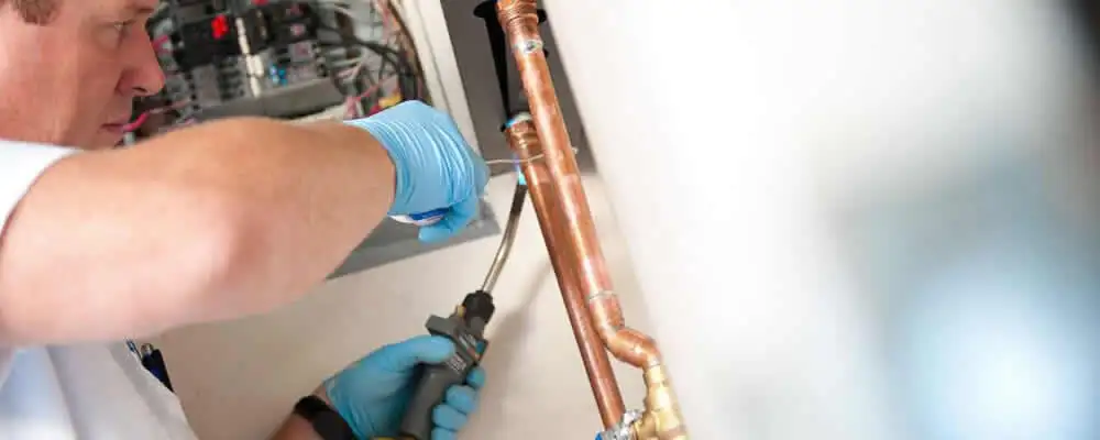 Water heater repair technician testing copper pipe connections and controls in Evansville, IN